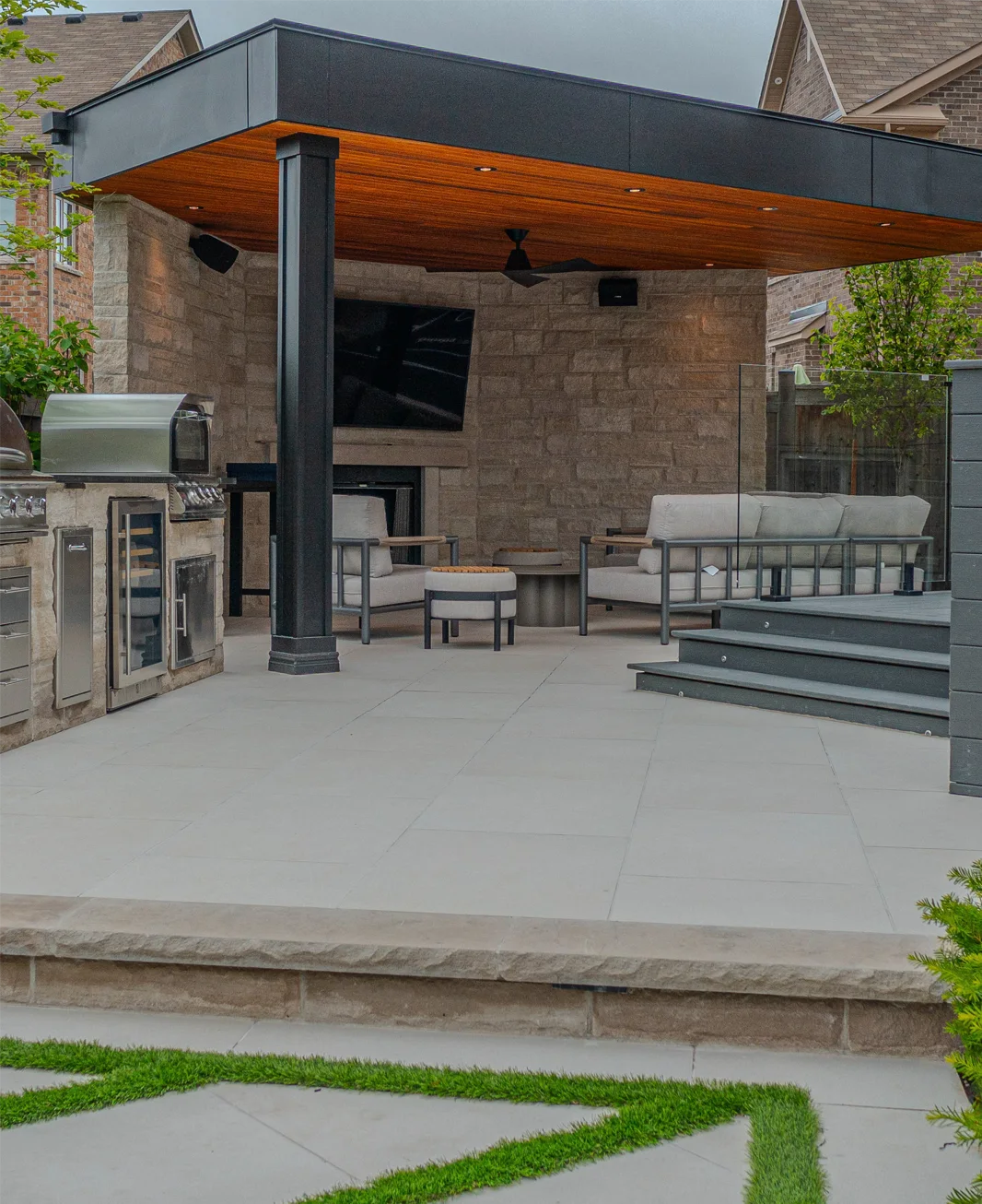 A backyard porcelain patio and a entertainment structure with a TV in it installed by Mutti Landscaping